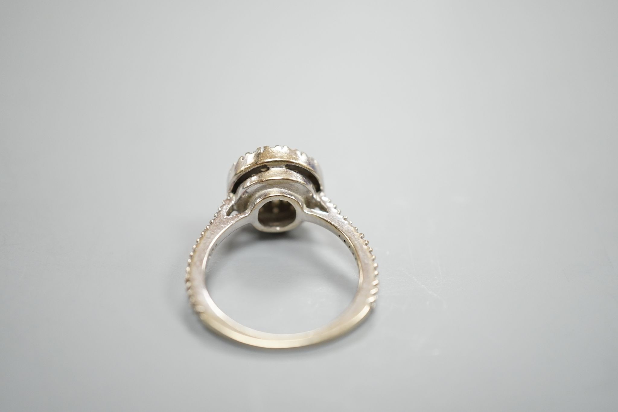 A modern white metal, round and trapeze cut diamond set target cluster ring, with diamond set shoulders, size N, gross weight 4.2 grams.
